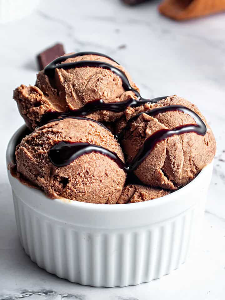 White bowl with chocolate ice cream and fudge. White marbled surface.