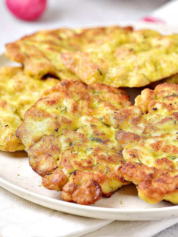 Close up overlapping chicken fritters on a white plate.