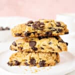 Three chocolate chip scones stacked on a white plate. Pink white background.