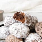 Pile of chocolate powdered sugar cookies, top one is bitten. White background.