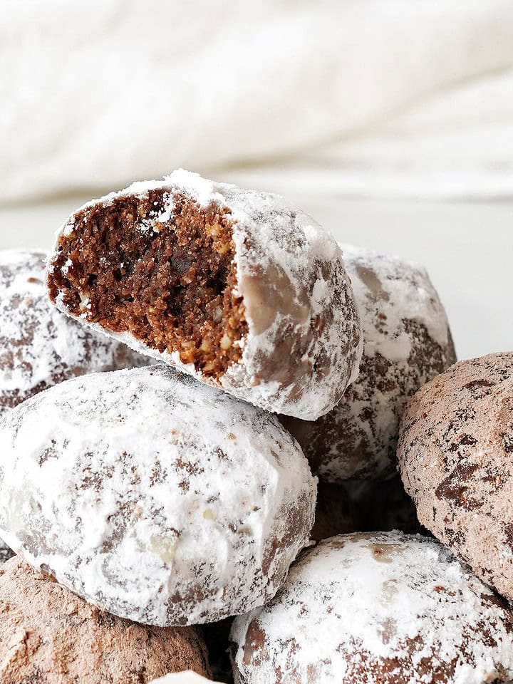 Pile of chocolate powdered sugar cookies, top one is bitten. White background.