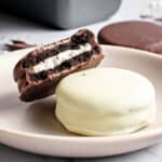 Whole white and bitten dark chocolate-covered Oreos in a pink plate.