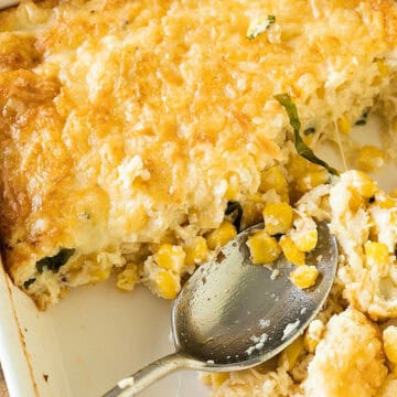 Close-up of white dish with corn pudding. Silver spoon inside, serving missing.