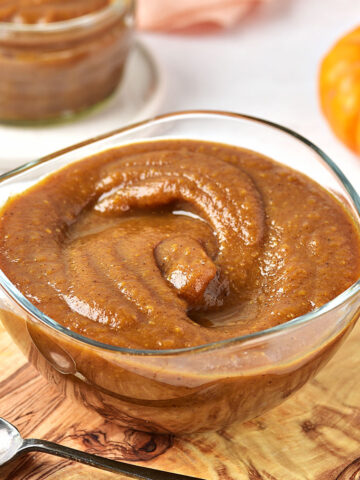 Glass bowl with pumpkin butter on a wooden board. A jar and small pumpkin on the white background.