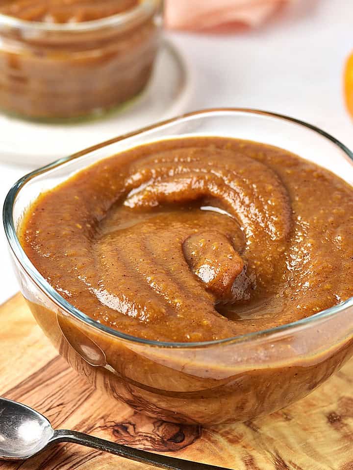 Glass bowl with pumpkin butter on a wooden board. A jar and small pumpkin on the white background.