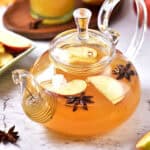 Close-up of spiced apple cider in a glass teapot. White gray surface.