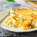 Blue cloth below a white plate with corn pudding serving. Silver fork.