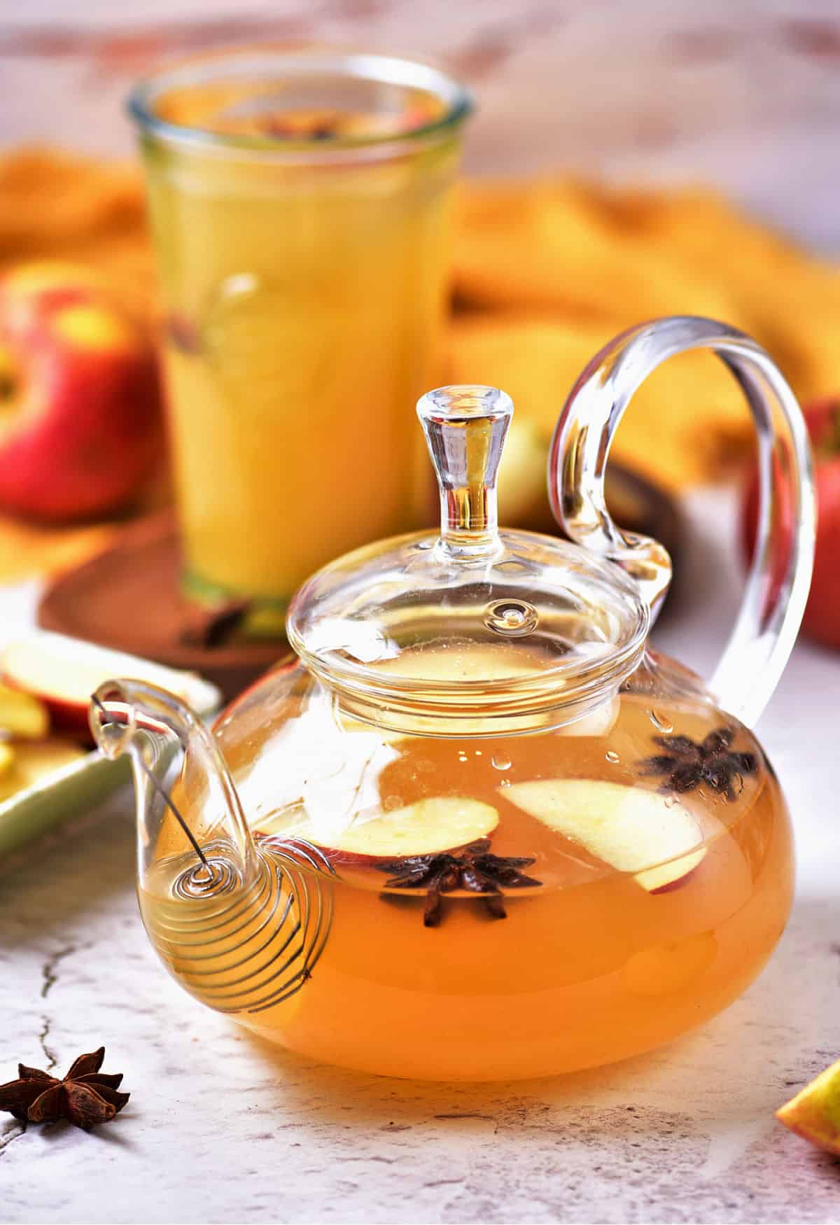 Apple cider with spices in a glass teapot. Cider glass in the yellow background.