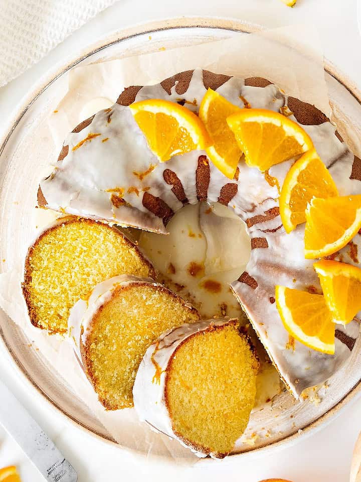 Top view of white plate with orange bundt cake with glaze. White background.