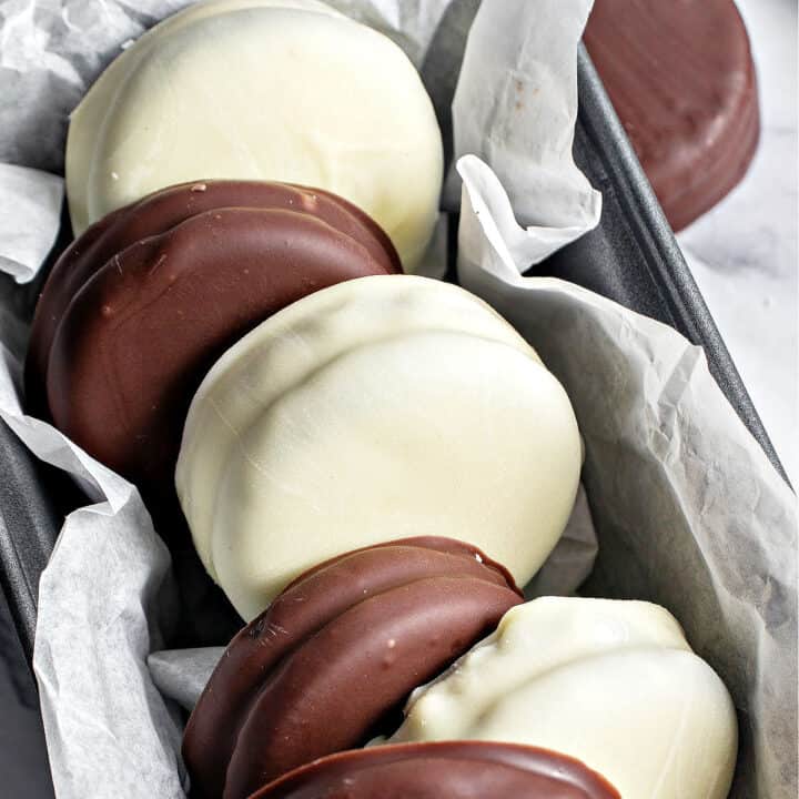 Alternating white and dark chocolate-covered Oreos on a loaf pan with parchment paper.
