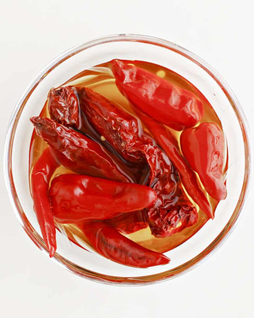 Dried chilies in water in a glass bowl. White background. Top view.