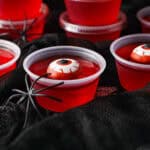 Red jello shots with candy eyes and spider. Black background.