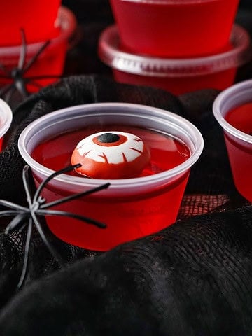 Red jello shots with candy eyes and spider. Black background.