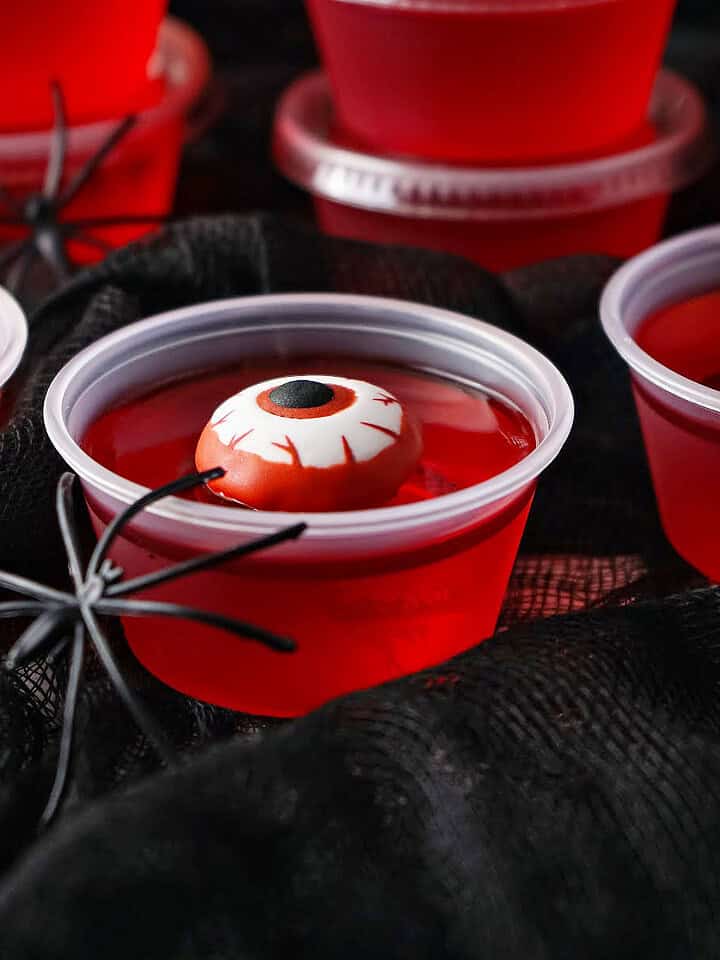 Red jello shots with candy eyes and spider. Black background.