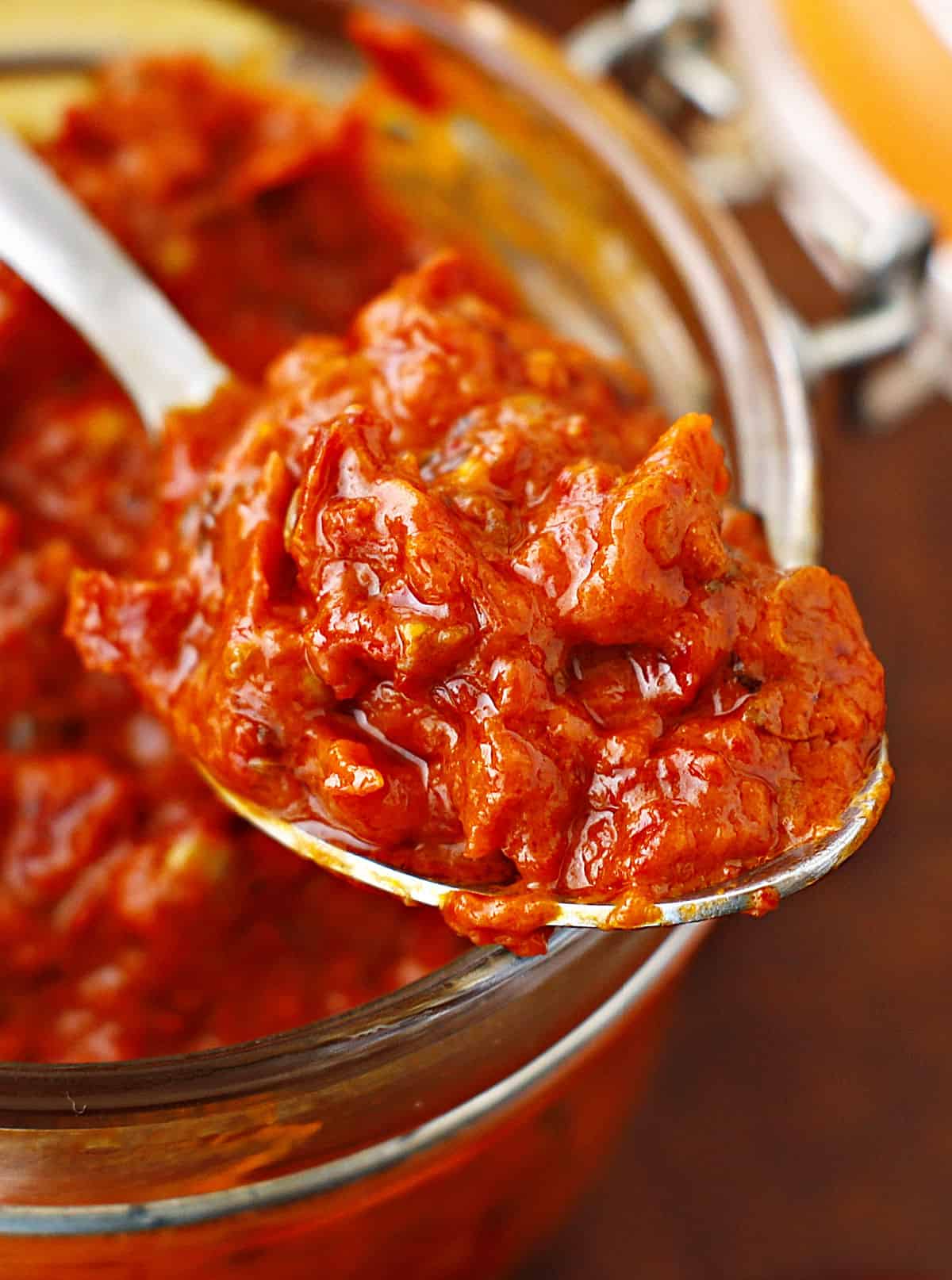 Silver spoon with harissa paste over a mason jar with the condiment.