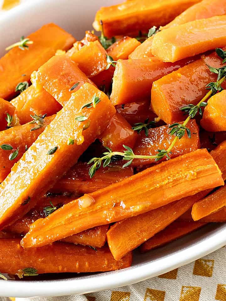 White oval dish with glazed carrots. Thyme sprigs. Gold dotted cloth.