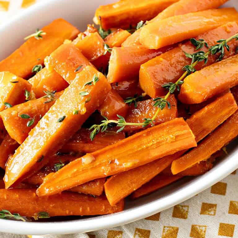 White oval dish with glazed carrots. Thyme sprigs. Gold dotted cloth.