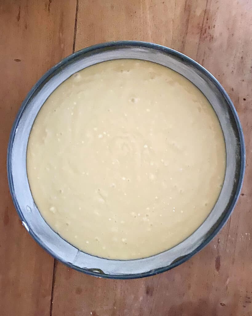 Wooden surface with round cake pan with ricotta batter. Top view.