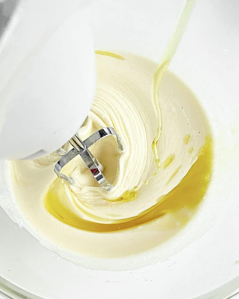 Beating oil into a vanilla cake batter in a glass bowl. 