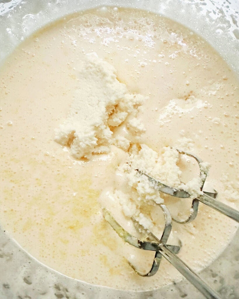 Glass bowl with beaters and ricotta cake batter being mixed.