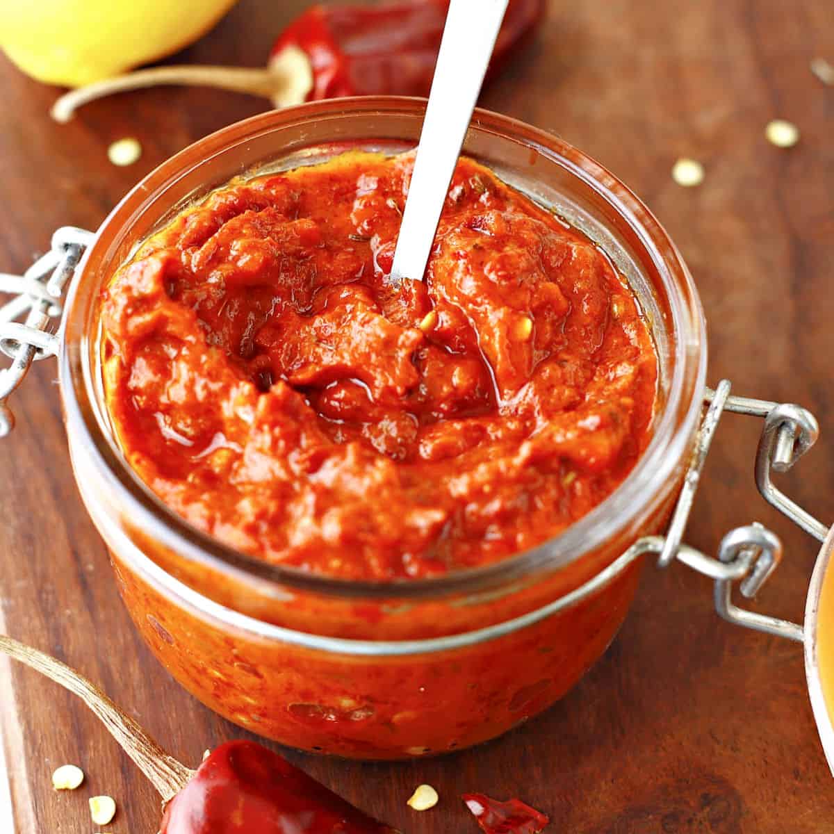 Jar with harissa paste on a wooden board. Silver spoon, dried chiles.