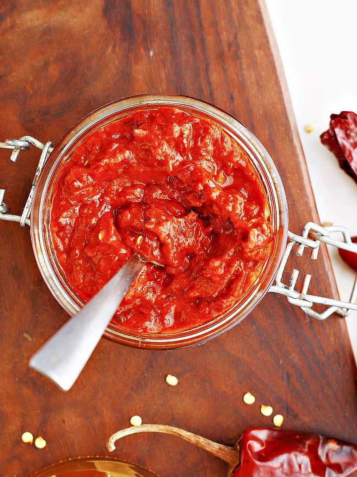 Wooden board with jar of harissa paste. Top view. Silver spoon, dried chilies.