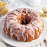 Vanilla glazed whole monkey bread on a gray plate and background. Gold cutlery, brown sugar jar.