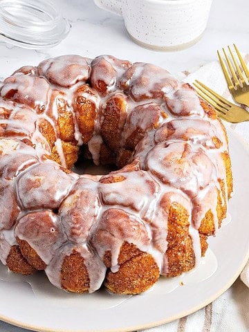 Vanilla glazed whole monkey bread on a gray plate and background. Gold cutlery, brown sugar jar.