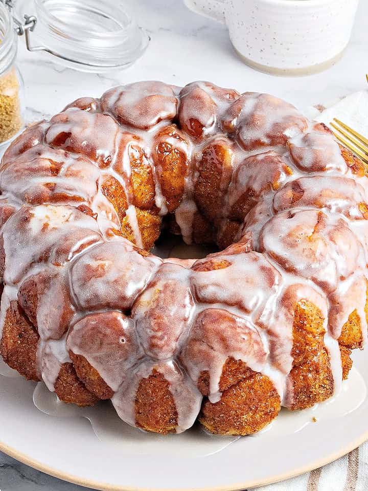 Vanilla glazed whole monkey bread on a gray plate and background. Gold cutlery, brown sugar jar.