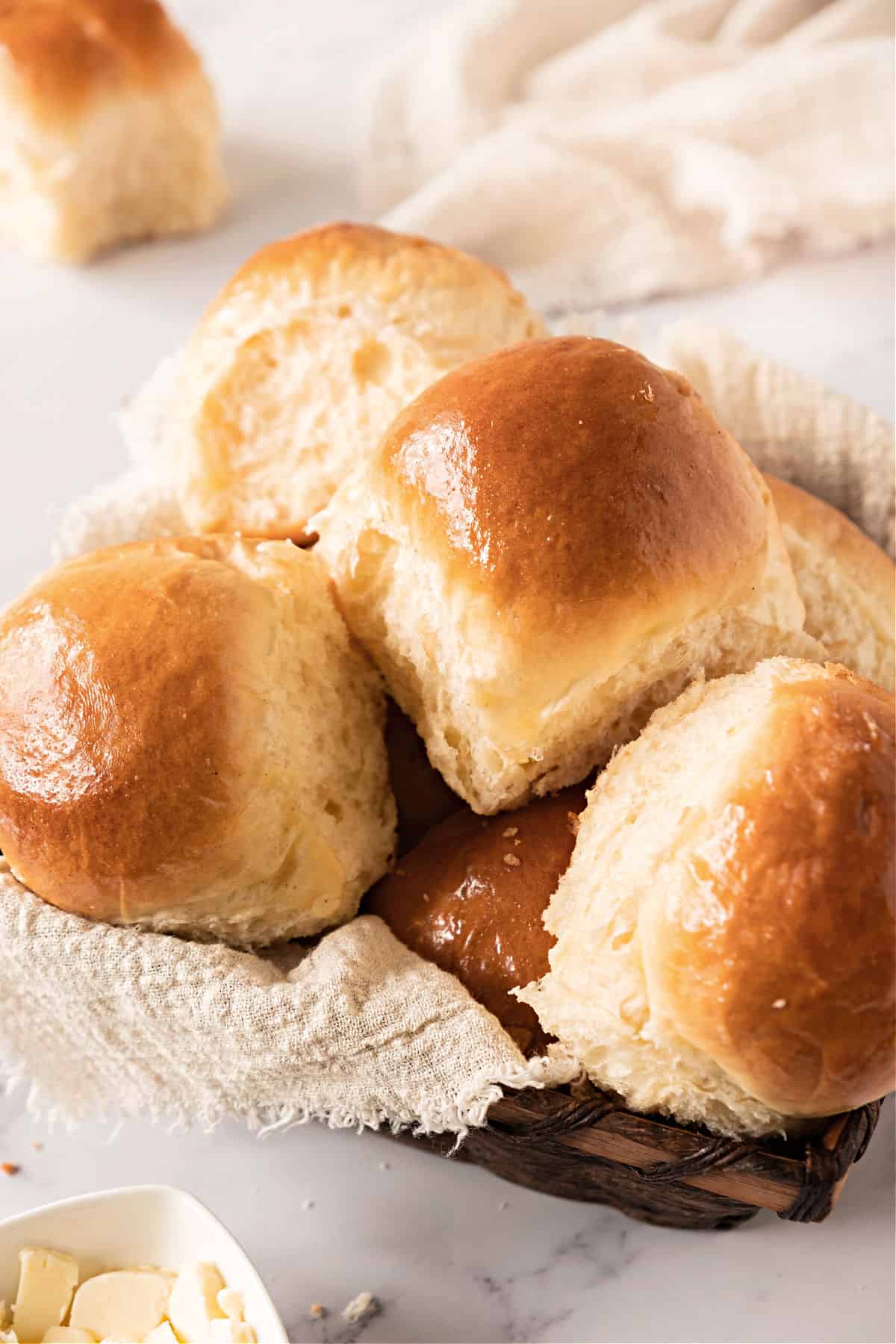 Several dinner rolls in a basket with beige cloth. White background.