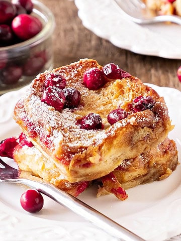 Serving of cranberry French toast on a white plate. Silver fork. Wooden surface.