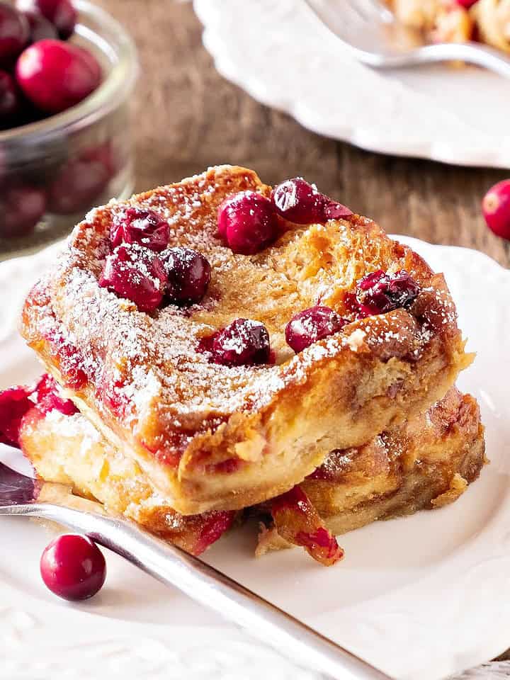 Serving of cranberry French toast on a white plate. Silver fork. Wooden surface.