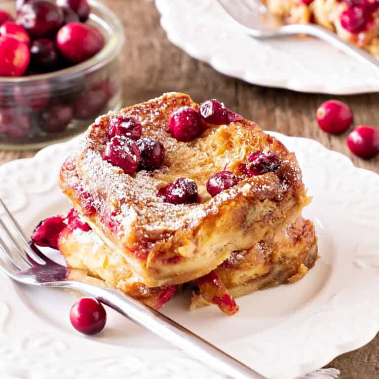 Serving of cranberry French toast on a white plate. Silver fork. Wooden surface.