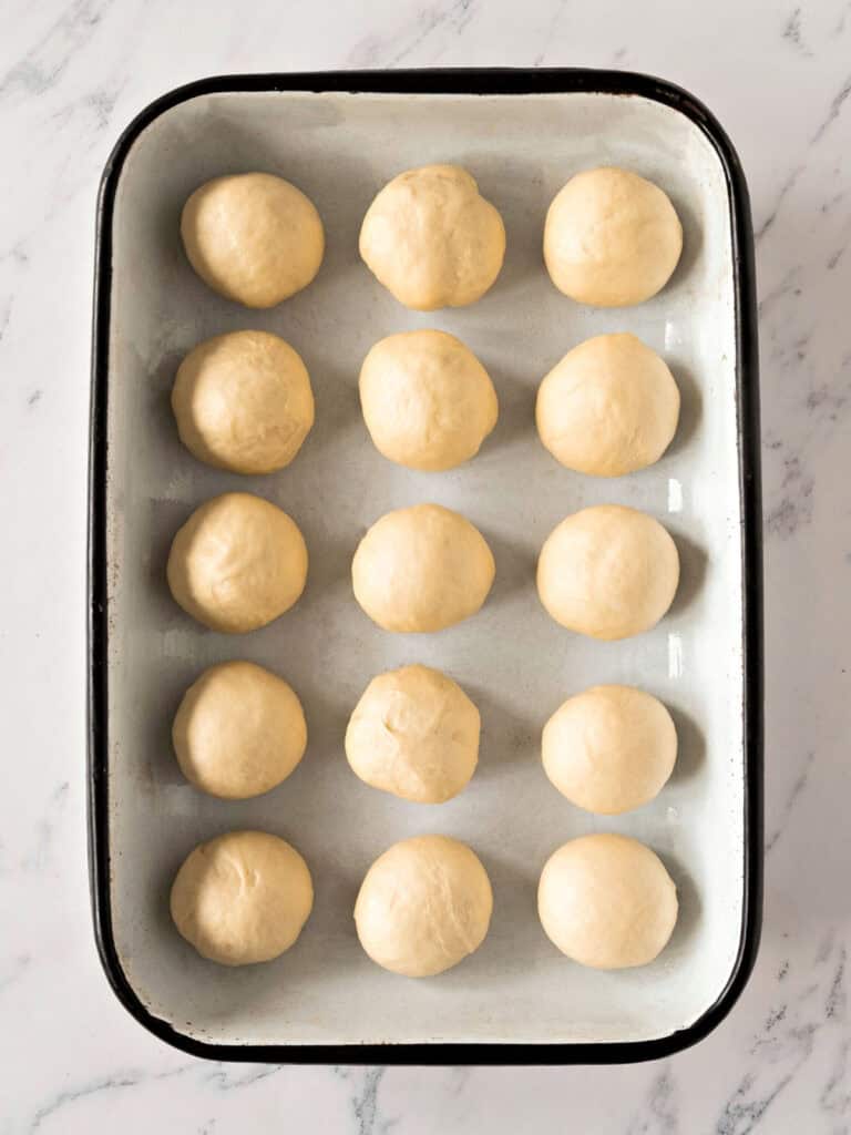 Rectangular enameled pan with white bread rolls. White marbled surface. Top view.