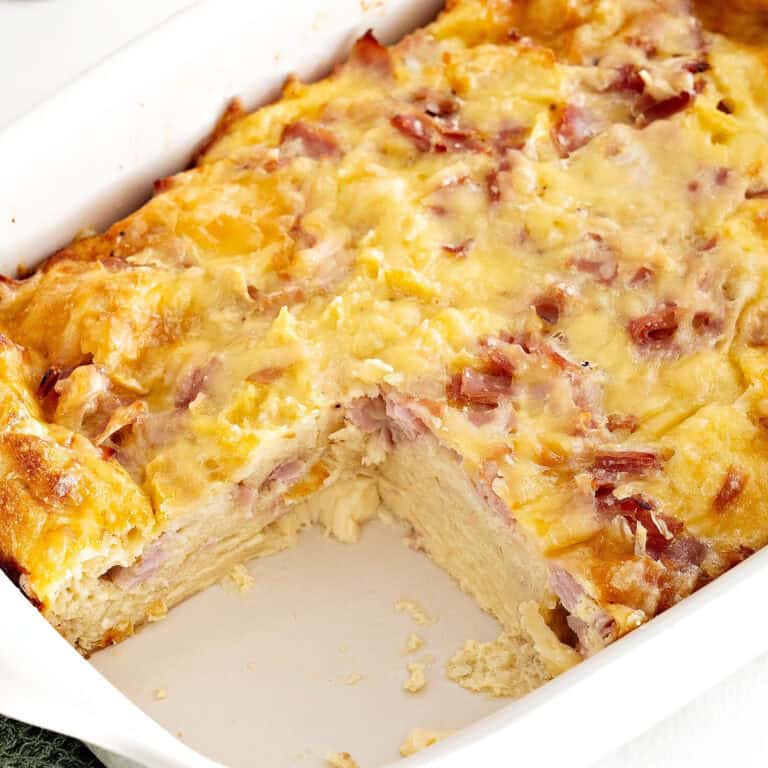 Bread pudding with ham and cheese in a rectangular baking white dish. Serving missing.
