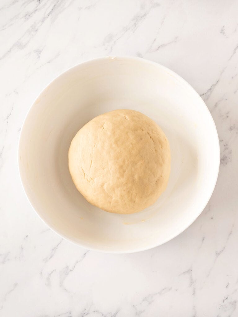 White bowl with bread dough. Top view. White marbled surface.