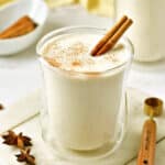 Glass of eggnog with cinnamon stick on a white board. Wooden spoon, anise stars.
