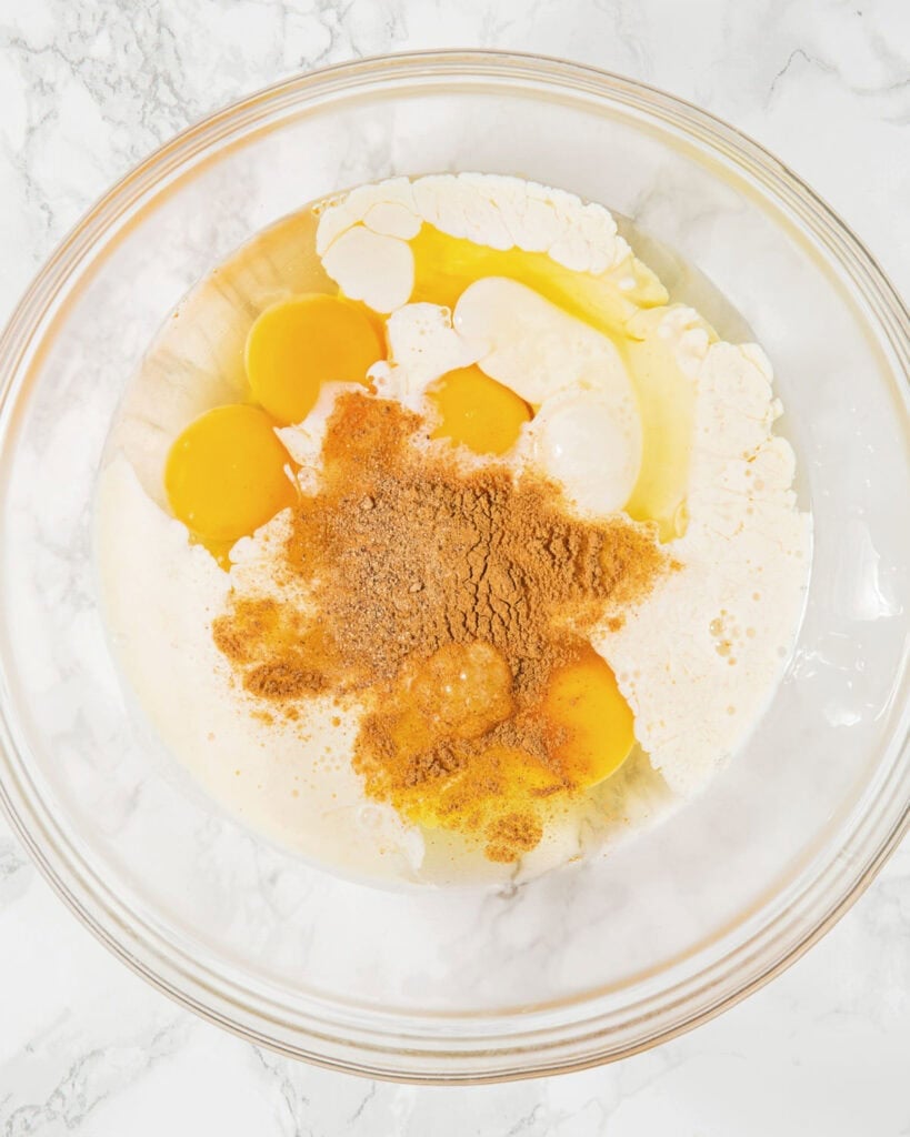 Egg, milk and spices in a glass bowl. White marbled background. Top view. 