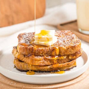 Three slices of French toast with butter and dripping syrup. White plate, Light wood background.