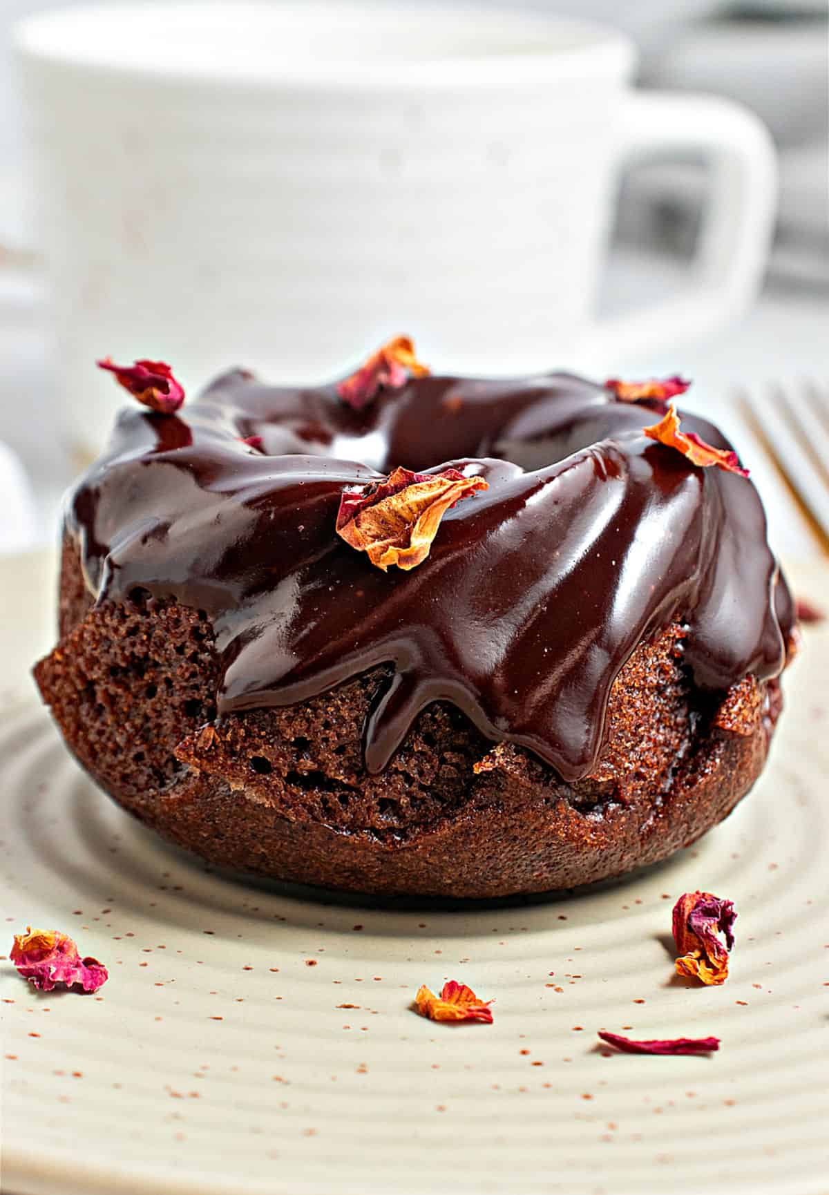 Single glazed chocolate small bundt cake on a greenish plate. Rose petals.