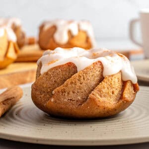 Single glazed mini pumpkin bundt cake on a dry green plate. More cakes in gray background.