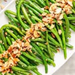 Close up of green beans with almond topping. White platter. Top view.