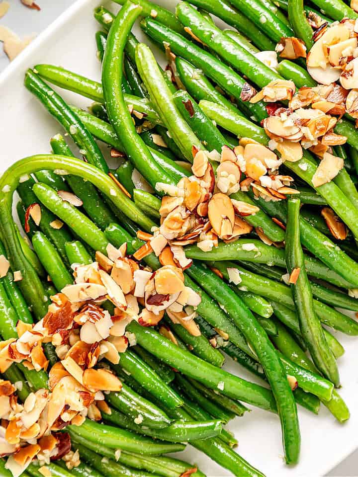 Close up of green beans with almond topping. White platter. Top view.