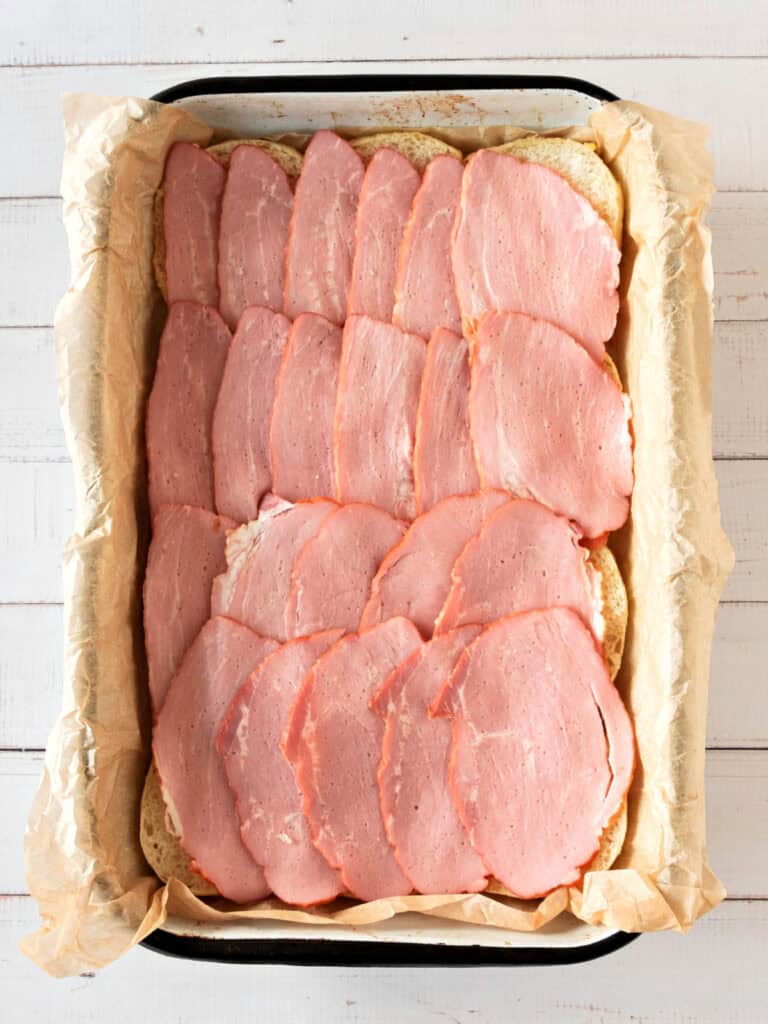 Rectangular dish with ham covered rows of small breads. White background. Top view.