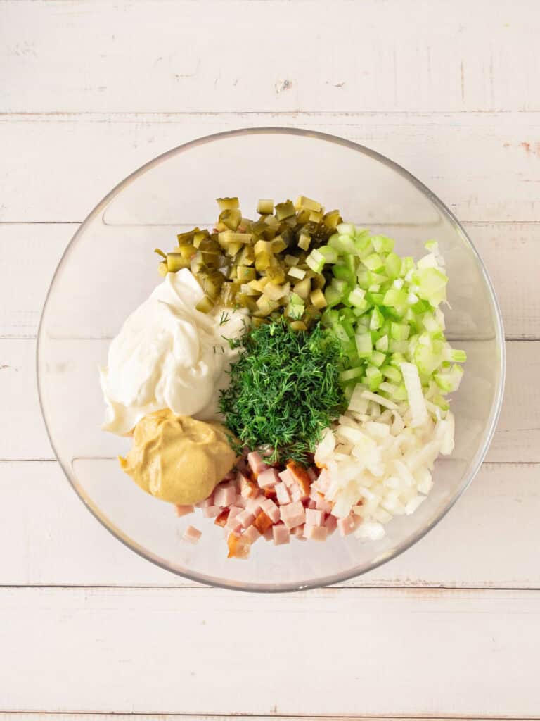 Glass bowl on a white striped surface with ingredients for ham salad. Top view.