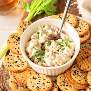 Ham spread in a white bowl. Silver spoon inside. Two-tone sesame crackers.