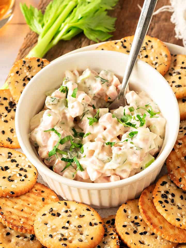 Ham spread in a white bowl. Silver spoon inside. Two-tone sesame crackers.