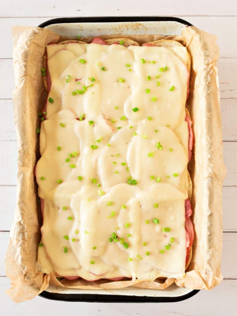 Top view of melted cheese layer on ham sandwiches in a enameled dish. White background.