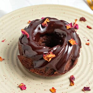 Rose petals sprinkled on chocolate glazed mini bundt cake. Greenish plate.