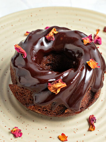 Rose petals sprinkled on chocolate glazed mini bundt cake. Greenish plate.